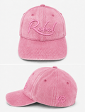 A pink washed cotton baseball cap shown from the front and side angles against a light gray background. The front features the word 'Rebel' embroidered in pink script, and the side displays a small Anarchy inspired embroidered 'R' logo.