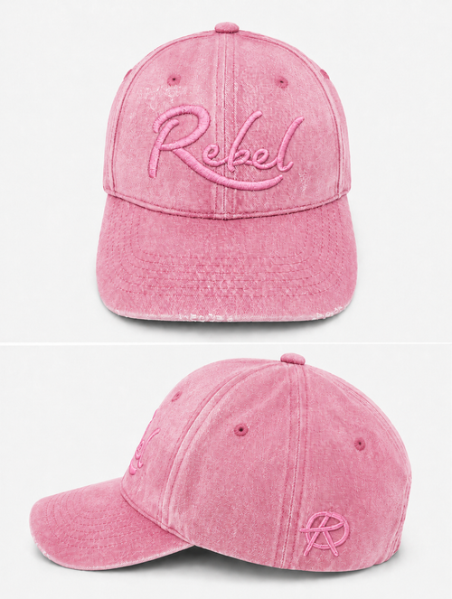 A pink washed cotton baseball cap shown from the front and side angles against a light gray background. The front features the word 'Rebel' embroidered in pink script, and the side displays a small Anarchy inspired embroidered 'R' logo.