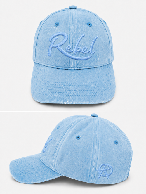 A light blue washed cotton baseball cap shown from the front and side angles against a light gray background. The front features the word 'Rebel' embroidered in light blue script, and the side displays a small Anarchy inspired embroidered 'R' logo.